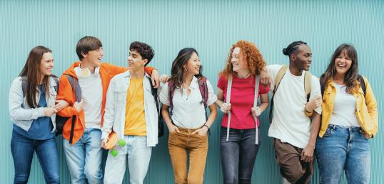 Diverse young people standing together in front of blue wall - Photo portrait of teenagers laughing together - Banner and 16:9 people background